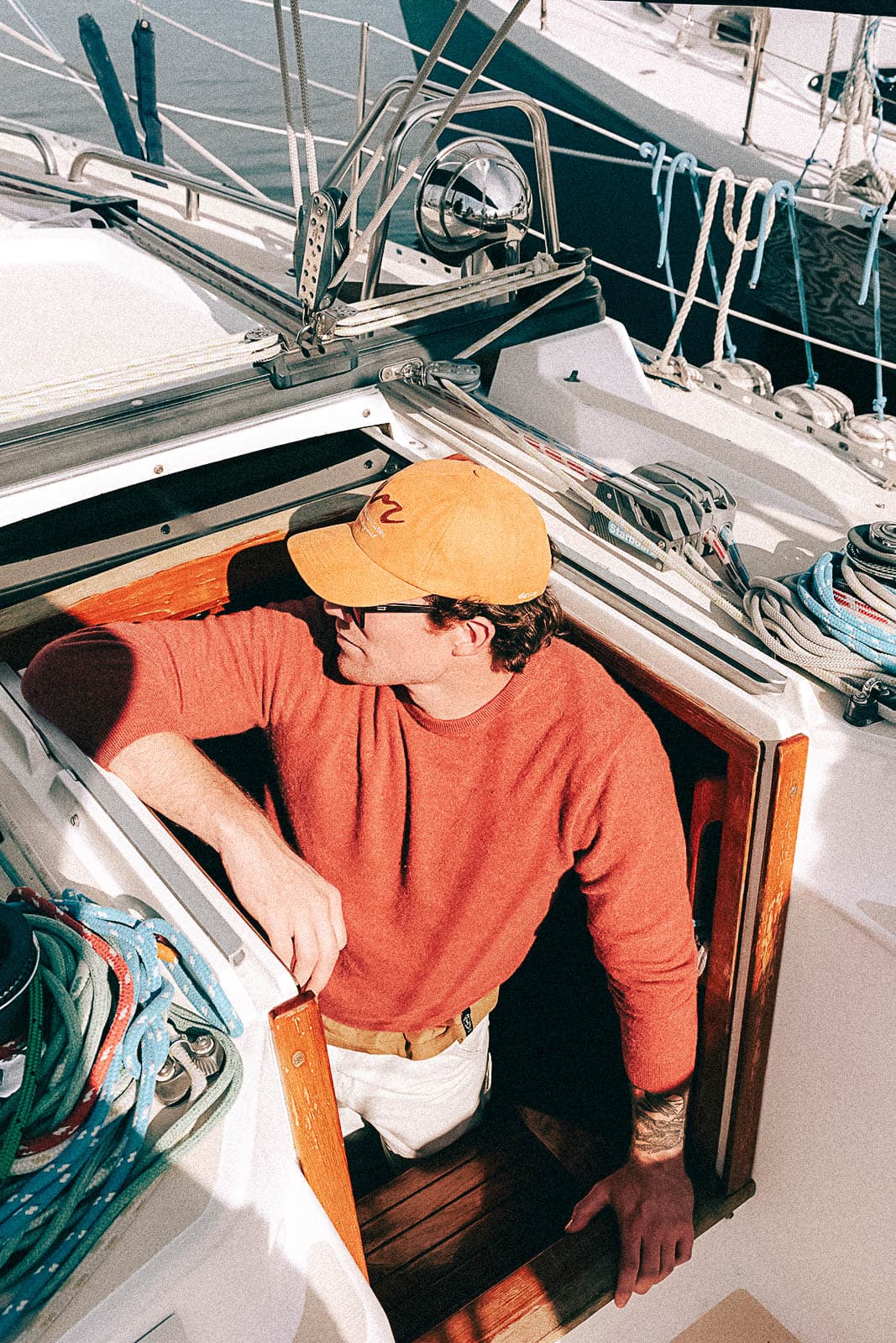 A person in an orange EVR cap and rust sweater aboard a sailboat
